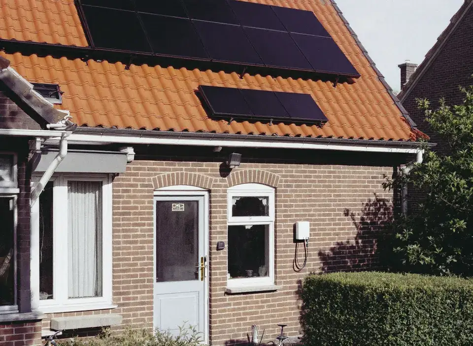 Een bakstenen rijtjeshuis met zonnepanelen op het oranje pannendak en een witte laadpaal naast de voordeur